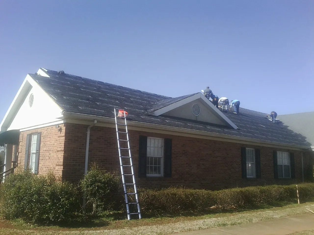 Crew tearing shingles off a brick ranch roof with a ladder set — Emergency Roof Repair work by our crew in Madras