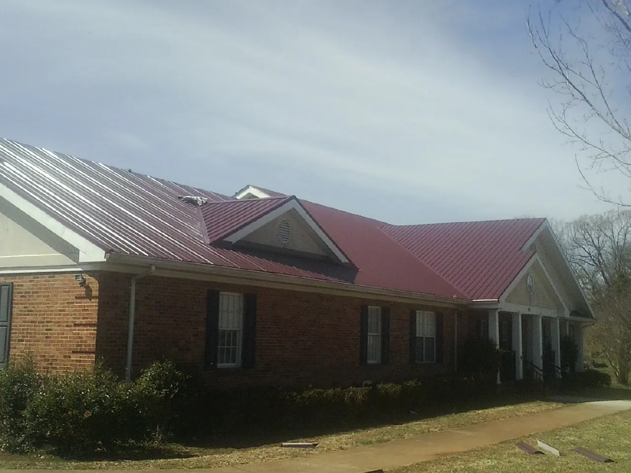 Red metal roof with gabled entries on a long brick building, from a Hail Damage Roof Repair job in Madras