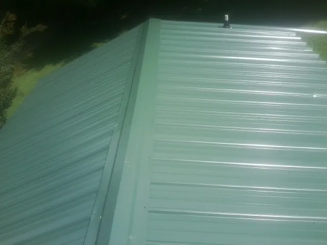 New green metal panels meeting at the ridge of a roof — Flat Roof Repair work by our crew in Madras