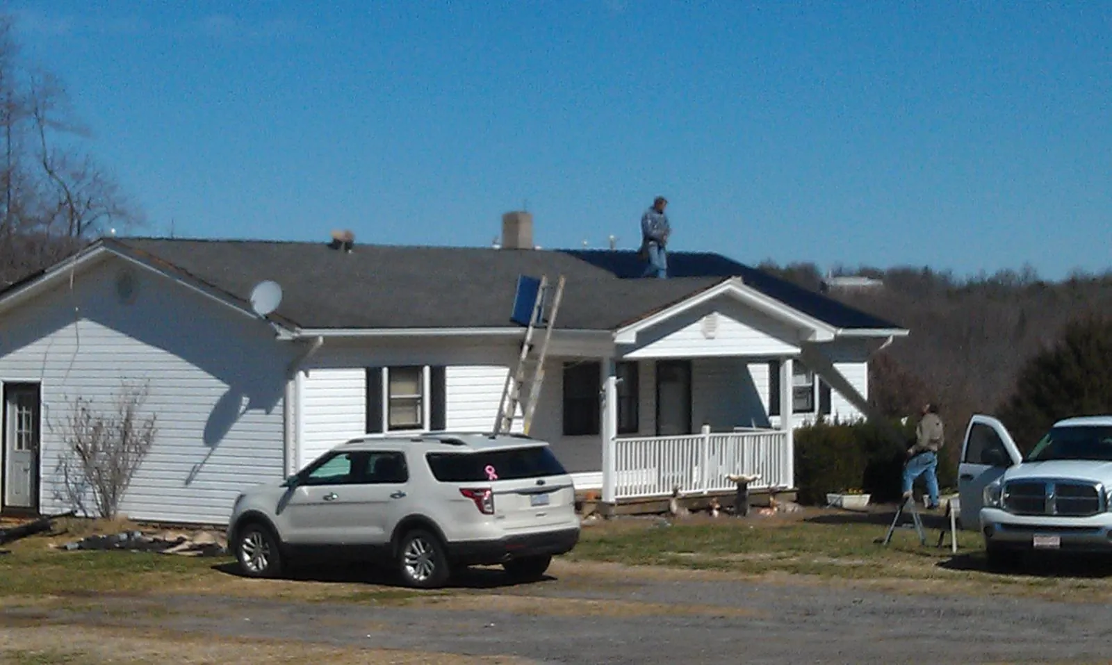 Roofers stripping shingles from a white ranch house roof in Madras